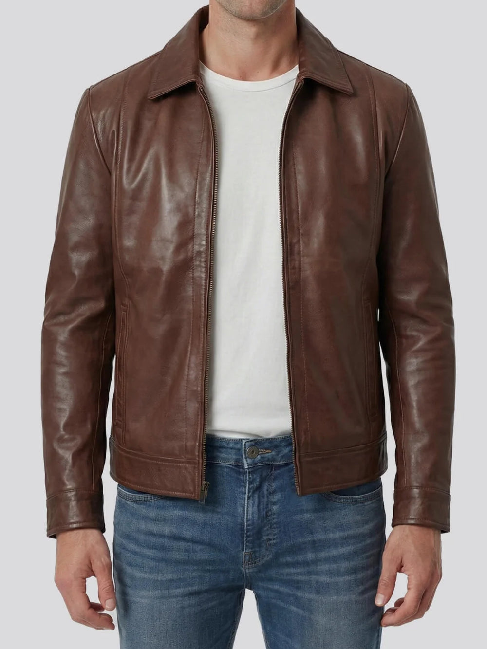 Man wearing a brown leather jacket over a white shirt and blue jeans on a light gray background